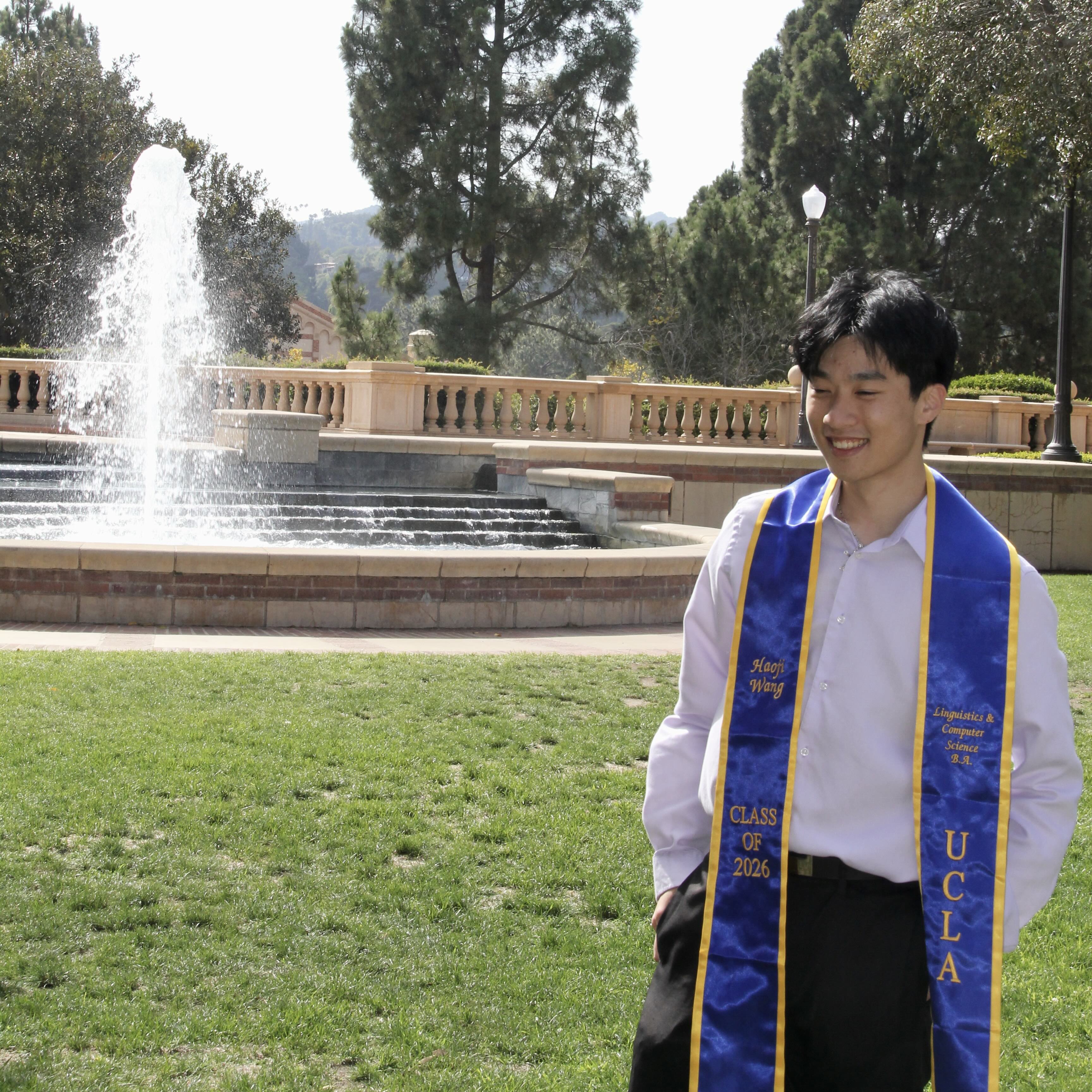 Haoji in graduation regalia by a campus fountain