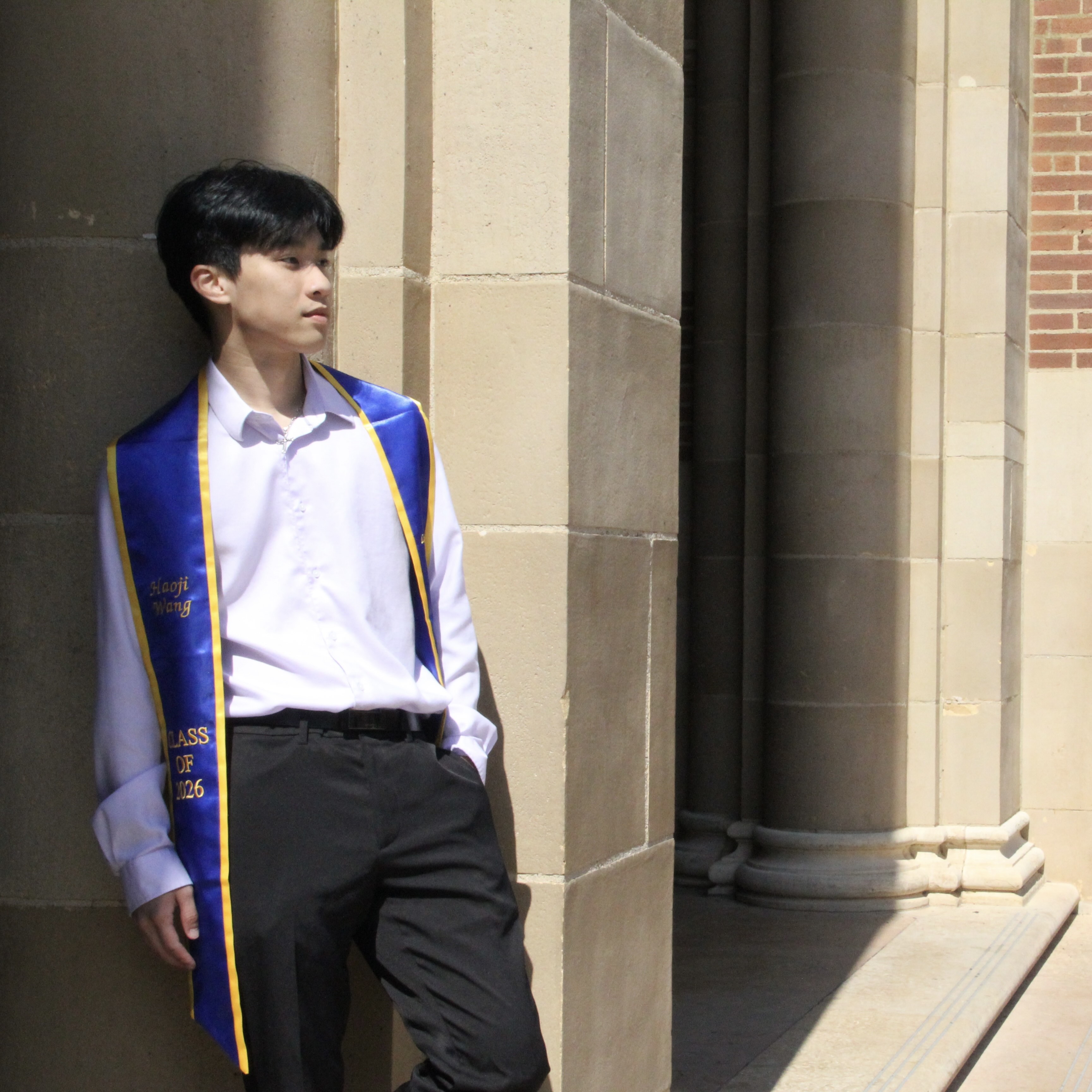 Haoji in graduation regalia beside a campus archway